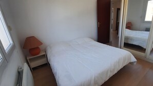 Quarto com cama, mesa de cabeceira, luminária, espelho e janela.