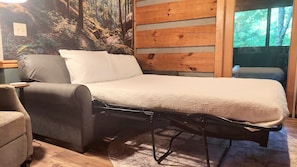 A bed with a white quilt, a grey sofa, and a wooden wall with a forest mural. - Mountain getaway 6 mins to attractions + 2 king beds + hot tub + fire pit (Sevierville)
