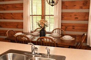 A wooden dining table set with plates, a vase of flowers, and chairs. - Mountains 6 mins to attractions + 2 king beds + hot tub + fire pit + pool access (Sevierville)