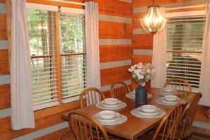 A dining room with a wooden table set for six, surrounded by chairs, with a vase of flowers on the table. - Mountain getaway 6 mins to attractions + 2 king beds + hot tub + fire pit (Sevierville)