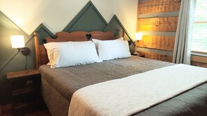 A neatly made bed with a headboard, two bedside lamps, and a wooden headboard with a heart-shaped cutout. - Mountains 6 mins to attractions + 2 king beds + hot tub + fire pit + pool access (Sevierville)