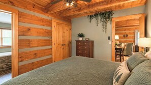 A bedroom with a bed, wooden walls, a dresser, a plant, and a desk with a chair. - Mountain getaway 6 mins to attractions + 2 king beds + hot tub + fire pit (Sevierville)