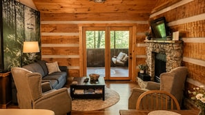 A cozy cabin interior with a stone fireplace, a sofa, and a television mounted on the wall. - Mountains 6 mins to attractions + 2 king beds + hot tub + fire pit + pool access (Sevierville)