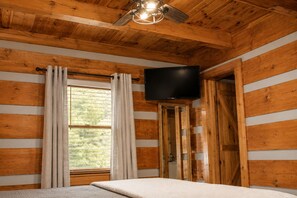 A room with wooden walls, a bed, a television, and a window with curtains. - Mountain getaway 6 mins to attractions + 2 king beds + hot tub + fire pit (Sevierville)