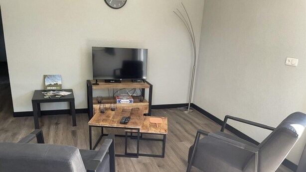 A living room with a TV, a coffee table, two chairs, a small table with a book, and a floor lamp. - Beautiful Accommodation in De Kiel (De Kiel)