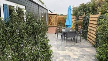 A patio with a table and chairs, surrounded by greenery and a wooden fence.