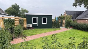 A green house with a paved pathway leading to it, surrounded by greenery and a wooden fence. - Beautiful Accommodation in De Kiel (De Kiel)