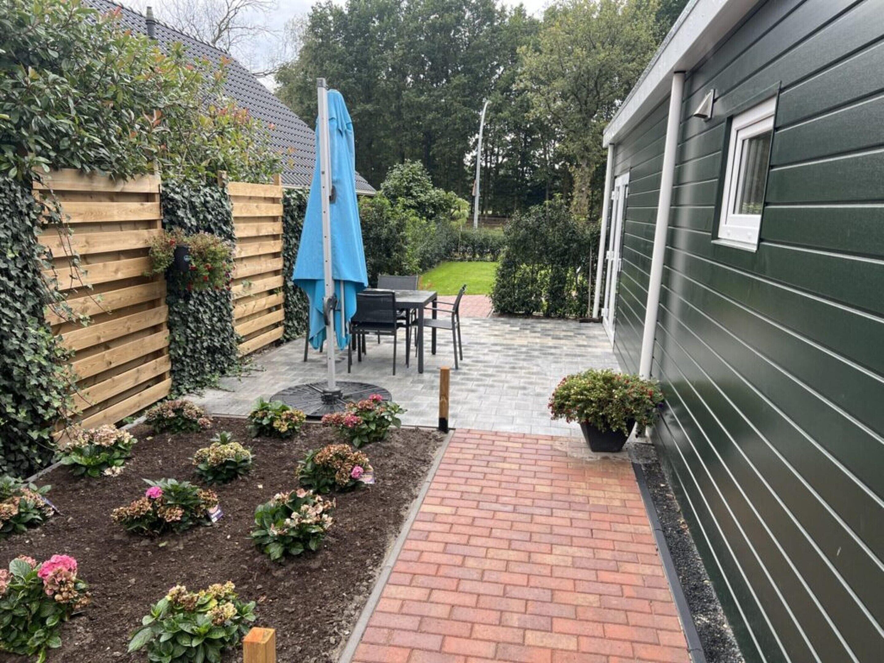 A patio with a brick pathway leading to a table and chairs, surrounded by a wooden fence and a green building.