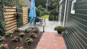 A patio with a brick pathway leading to a table and chairs, surrounded by a wooden fence and a green building. - Beautiful Accommodation in De Kiel (De Kiel)
