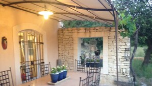 Un patio exterior con muros de piedra, una mesa, sillas y plantas en macetas.