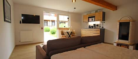 A bedroom with a bed, a TV, a kitchenette, and a view of the outdoors.