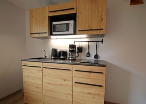 A kitchen with wooden cabinets, a microwave, a coffee maker, and utensils hanging on the wall. - Neues Appartement Nr. 6 im Lepels Hof (Luetow)