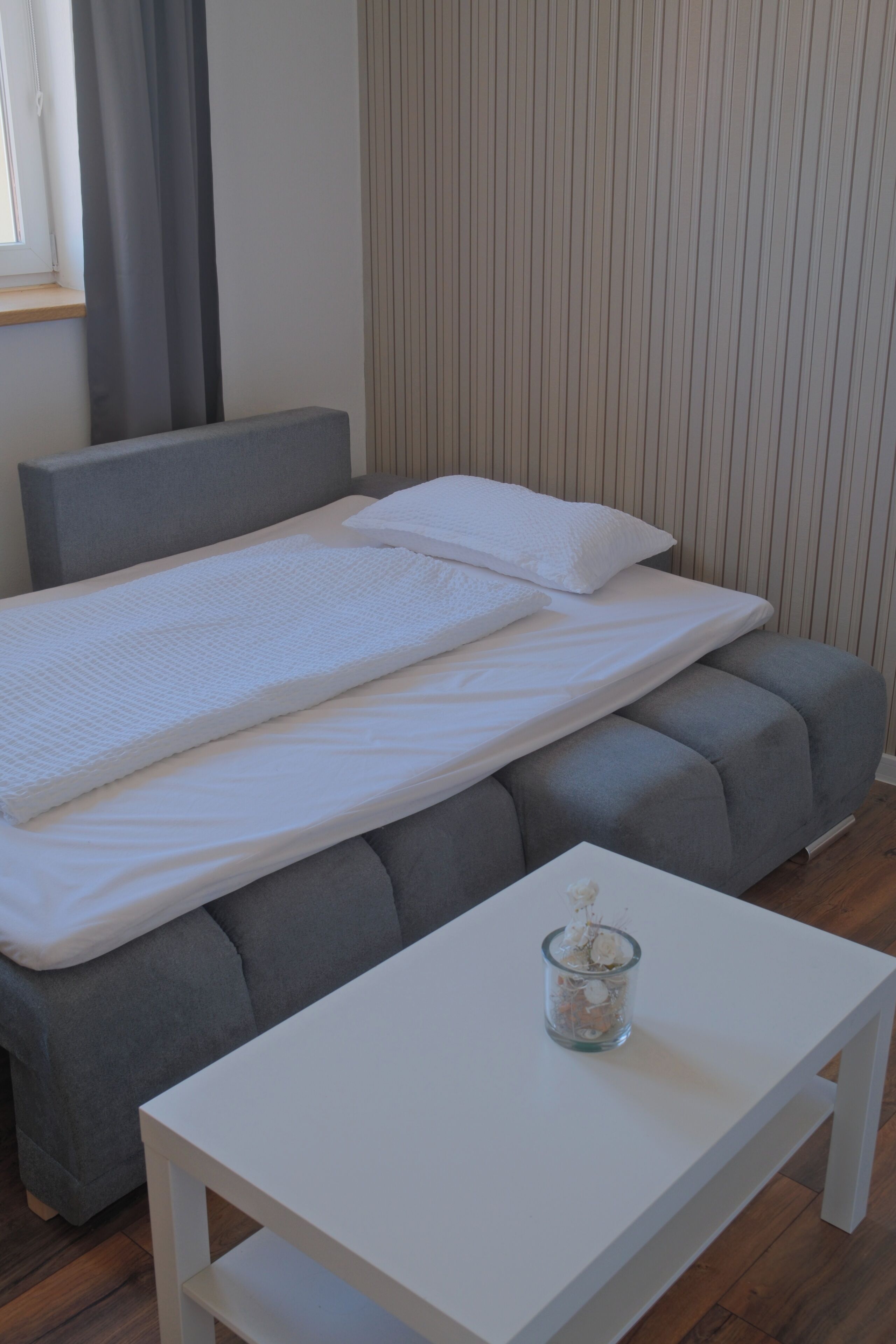 A neatly made bed with a gray headboard, a white pillow, and a white mattress cover.