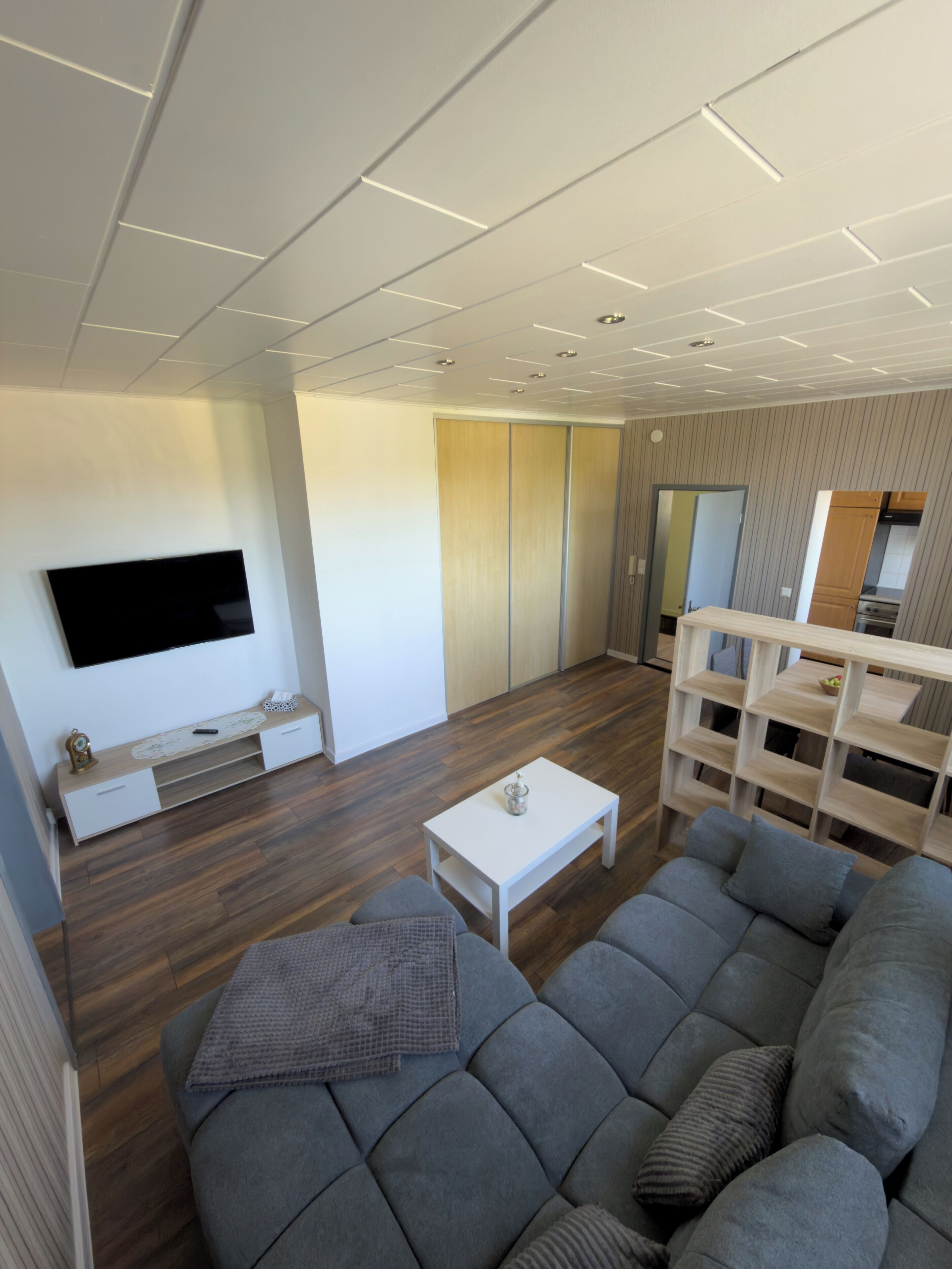 Un salon moderne avec un téléviseur à écran plat, une table basse blanche, un canapé gris et un meuble en bois.