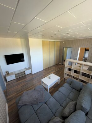 A modern living room with a flat-screen TV, a white coffee table, a grey sofa, and a wooden cabinet.