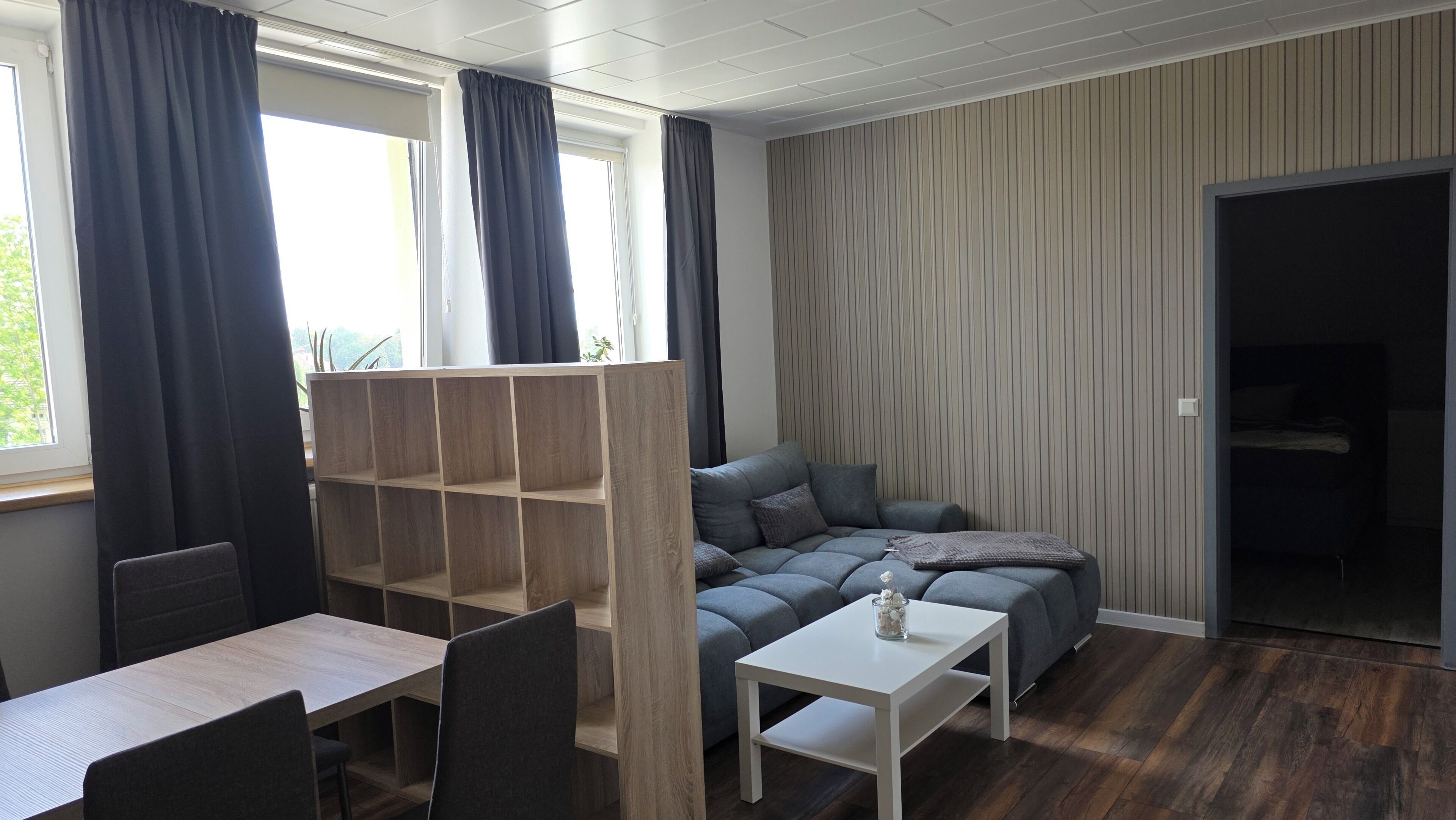 A modern room with a grey sofa, a white table, and a wooden shelving unit.