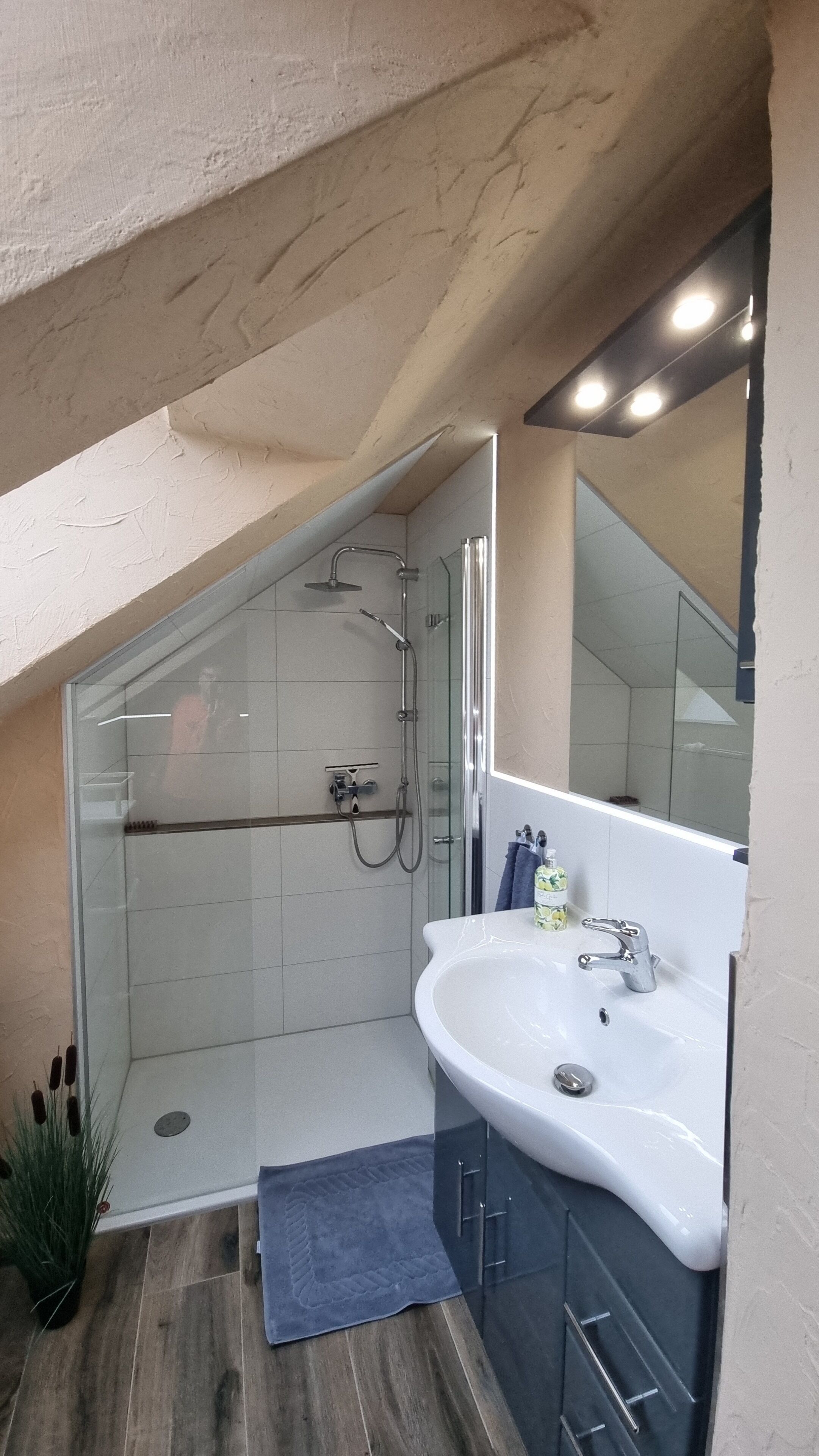 Ein modernes Badezimmer mit einer Duschkabine aus Glas, einem weißen Waschbecken und einem großen Spiegel.