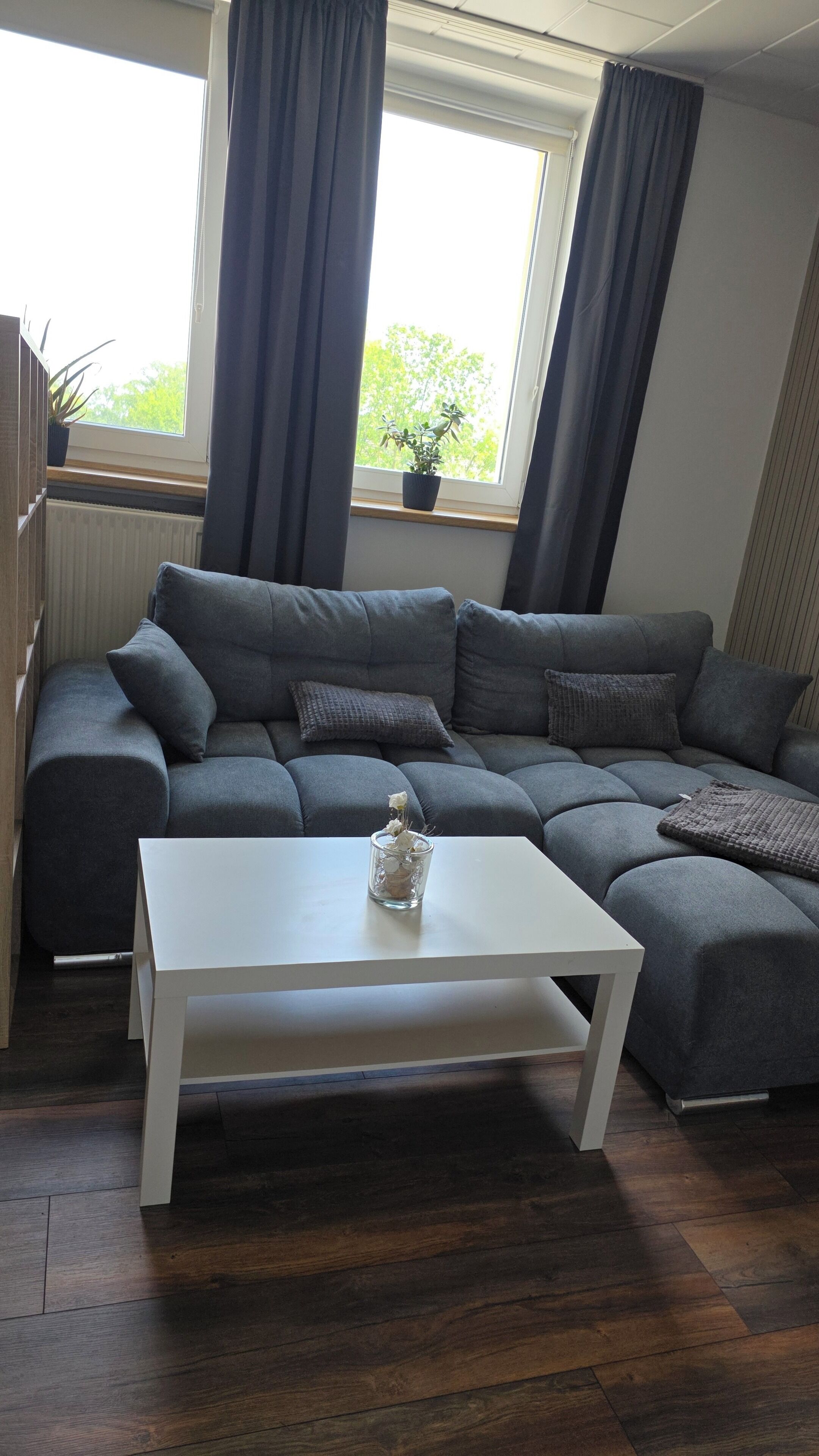 A modern living room with a grey sectional sofa, a white coffee table, and a window with curtains.