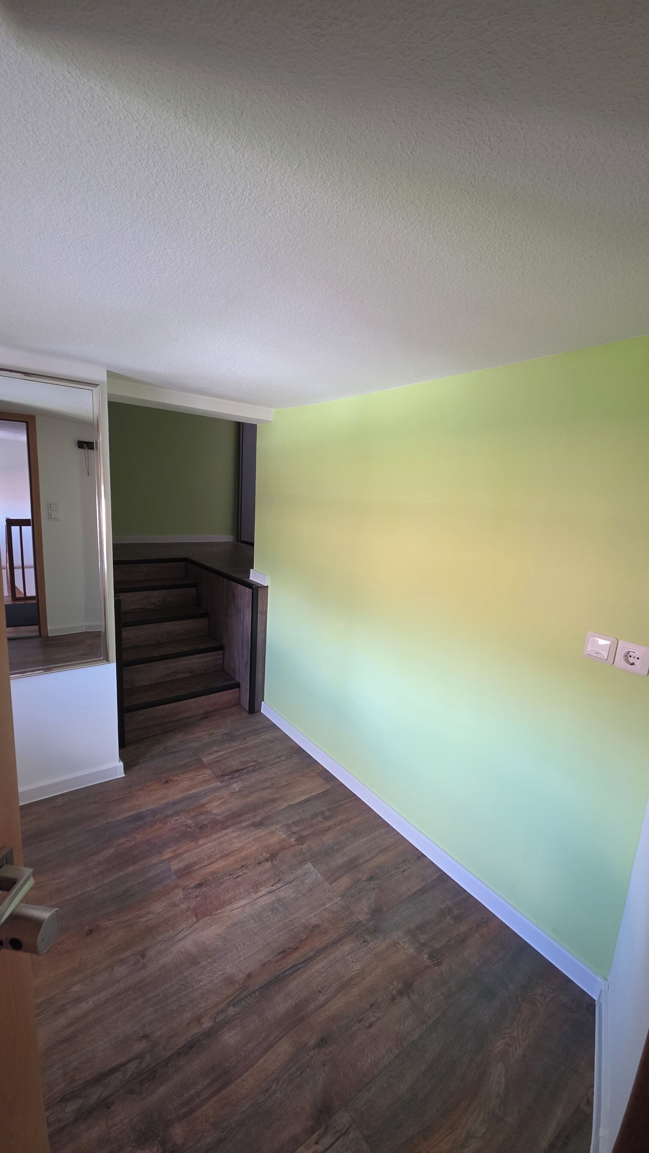 Ein Zimmer mit Holzboden, einer Treppe und einer grünen Wand.