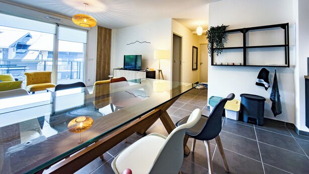 Habitación de hotel moderna con una mesa de comedor de vidrio, asientos cómodos, un televisor de pantalla plana y vista a la ciudad.