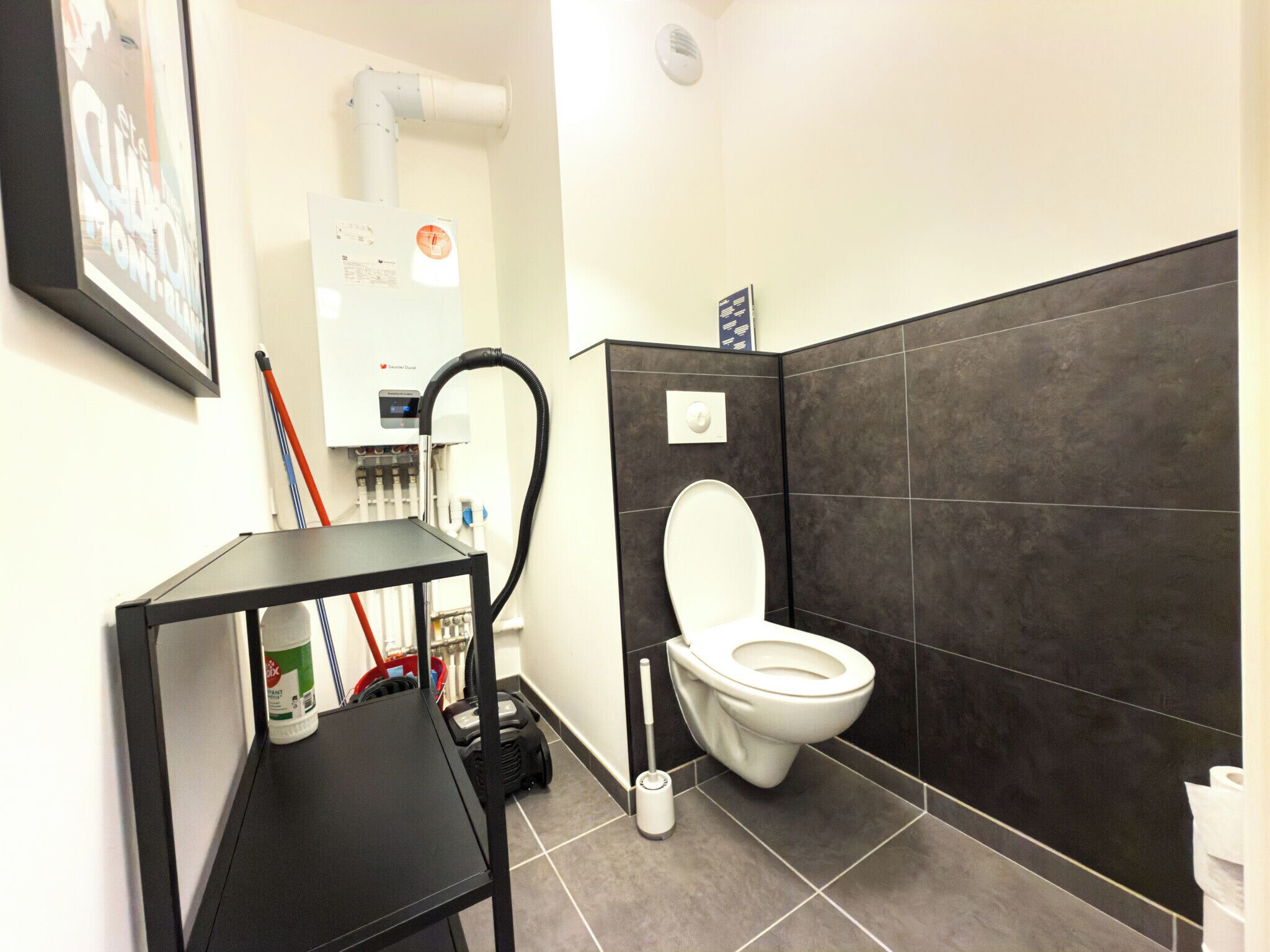 Une salle de bain moderne équipée de toilettes, d’une étagère à cadre noir, d’un aspirateur et d’un sèche-mains.