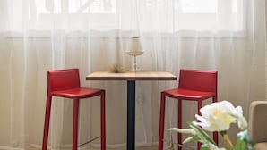 Een kamer met een tafel, twee stoelen, een lamp en een raam met dunne gordijnen.