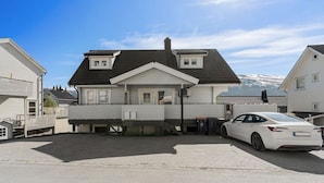 Een tweelaags huis met een garage, een witte auto op de oprit, en een berg op de achtergrond.