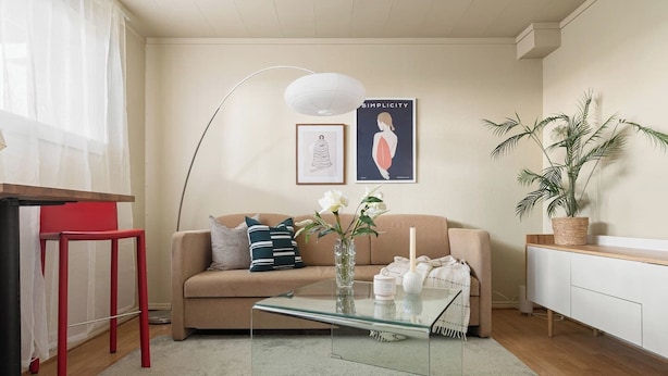 Een woonkamer met een bank, een glazen salontafel, een rode stoel, een witte kast en een potplant.
