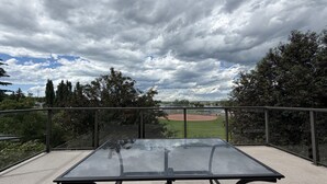 A glass-top table with metal legs, a view of a baseball field, and surrounding trees. - 4BR Calgary Home | Ping Pong + Parking (Calgary)