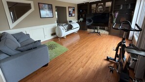 A living room with a grey sofa, a massage chair, a stationary bike, and a television. - 4BR Calgary Home | Ping Pong + Parking (Calgary)