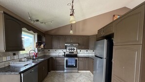 A kitchen with dark brown cabinets, a stainless steel refrigerator, a built-in oven, and a dishwasher. - 4BR Calgary Home | Ping Pong + Parking (Calgary)