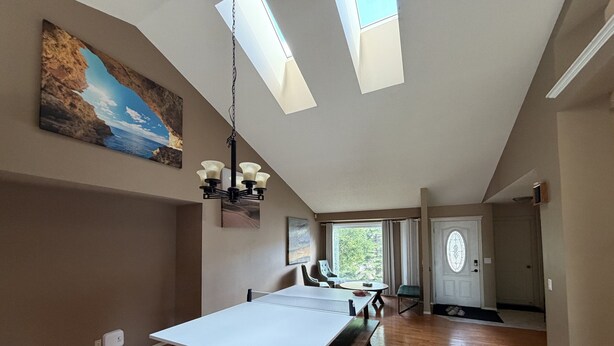 A spacious room with a dining table, a chandelier, and a large painting on the wall. - 4BR Calgary Home | Ping Pong + Parking (Calgary)