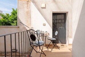 A balcony with two chairs and a small table, a door with a metal gate, and a white wall with a window. - Vecchia Bari Basilica San Nicola | Cozy Studio in Old Bari (Bari)