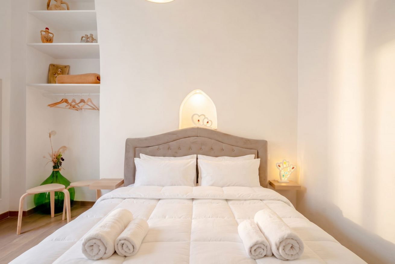 A neatly made bed with rolled towels, a wooden headboard, and a bedside table with a lamp.