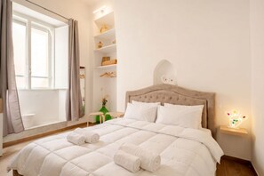 A bedroom with a bed, a bedside table with a light, and a window with curtains. - Vecchia Bari Basilica San Nicola | Cozy Studio in Old Bari (Bari)