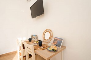 Ein Essbereich mit einem Holztisch, Stühlen, einem an der Wand montierten Fernseher und einem gerahmten Bild auf dem Tisch.