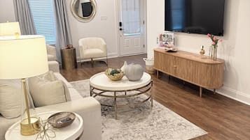 A modern living room with a sofa, a round coffee table, a TV mounted on the wall, and a ceiling fan.
