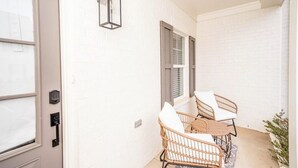 A corridor with white brick walls, a door with a keypad lock, and two wicker chairs with white cushions. - The Rebel Retreat -Oxford's Home Base for Every Rebel Adventure (Oxford)