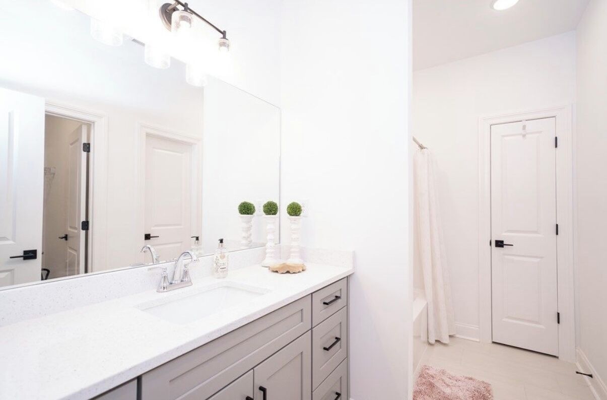 A bathroom with a white sink, mirror, and two small potted plants on the counter.