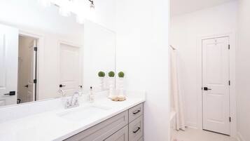 A bathroom with a white sink, mirror, and two small potted plants on the counter.