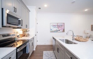 A modern kitchen with white cabinetry, stainless steel appliances, and a large island with a sink. - The Rebel Retreat -Oxford's Home Base for Every Rebel Adventure (Oxford)