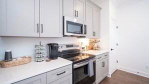 A modern kitchen with white cabinets, a microwave, a stove, and a coffee maker. - The Rebel Retreat -Oxford's Home Base for Every Rebel Adventure (Oxford)
