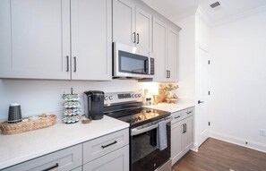 Una cucina moderna con pensili e basi bianche, un forno a microonde, un fornello e una macchina da caffè.