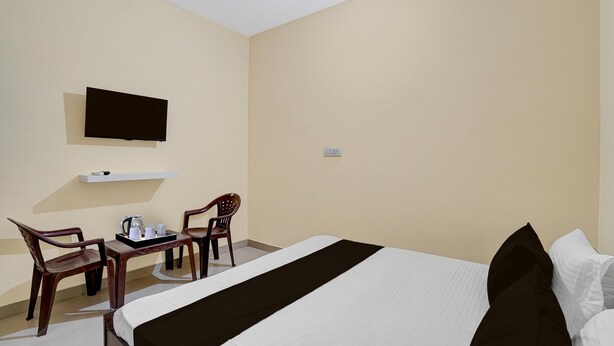 A hotel room with a bed, a television mounted on the wall, a small table with a tray of cups and a kettle, and two wooden chairs. - Deluxe Chandigarh Outer (Kharar)