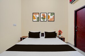 A hotel room with a bed, two nightstands, a red door, and three framed artworks on the wall. - Deluxe Chandigarh Outer (Kharar)