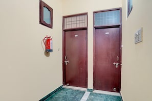 A hallway with two wooden doors, a fire extinguisher, and a small window. - Deluxe Chandigarh Outer (Kharar)
