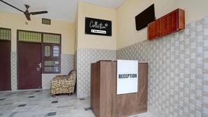 A reception area with a wooden desk, a reception sign, a ceiling fan, and a patterned wall. - Deluxe Chandigarh Outer (Kharar)