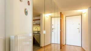 Un passadís amb un mur mirall, un radiador, una zona de cuina i una porta amb nassó.
