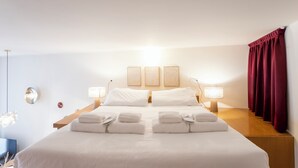 Una habitació d'hotel amb un llit gran, dues taules de nit, una làmpada penjada a la paret i una finestra amb cortines.