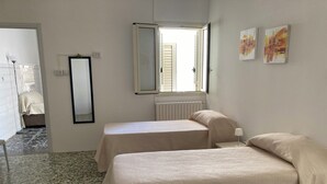 Une chambre avec deux lits, une fenêtre avec des stores, un radiateur et un miroir au mur.